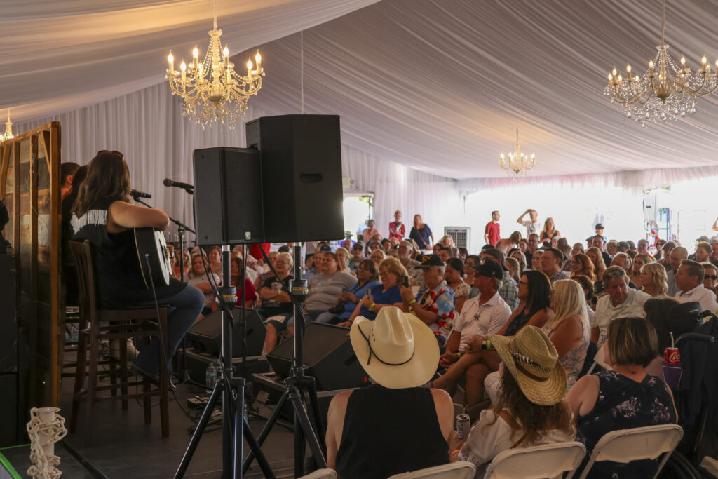 A crowd sitting inside of the Haggin Oaks Pavilion during the Singer/Songwriter performances. The room is packed and listening to the musicians.