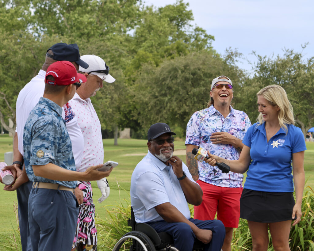 Jason Michael Carroll and members of PGA Hope are being interviewed by Molly Riehl from Good Day Sacramento. The man being interviewed is in a wheelchair while looking at the camera, Molly and Jason are laughing at a joke he made.