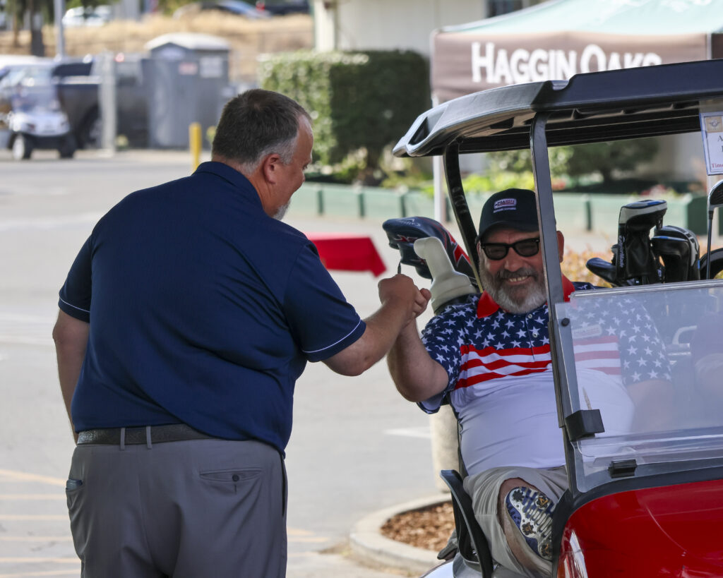 Ken Morton Jr. fist bumps a member of PGA Hope as he drives by in a golf cart to his starting hole.