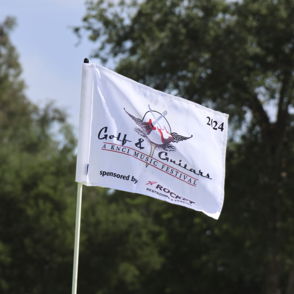 A close-up of a white golf flag with the Golf & Guitars logo.