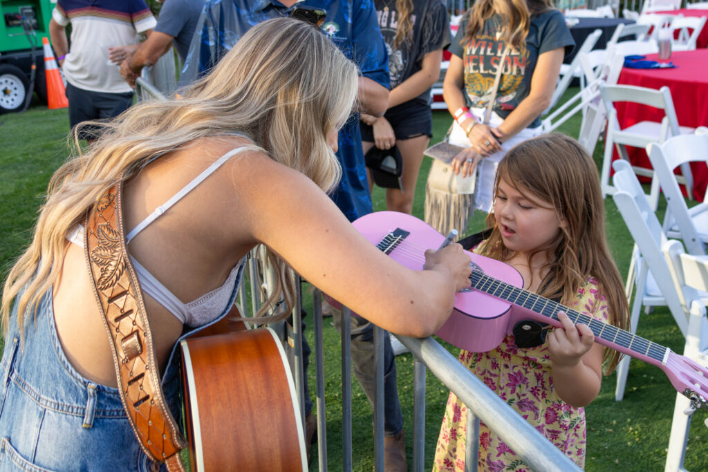 Ashely Cooke signing a young female fan's pink guitar.