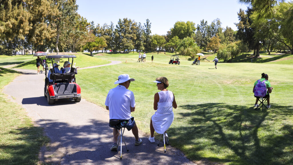 A crowd watches the final group at Bartley Cavanaugh. There are people walking, sitting on chairs, and following in golf carts.