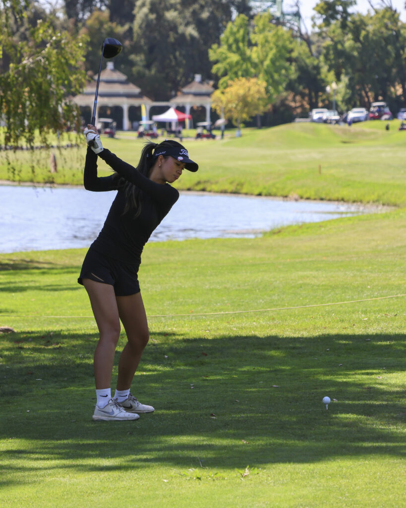 Erica Villegas is frozen mid-swing on the #18 tee box. She is about to bring down her driver and launch the ball over the water hazard and towards the green. 