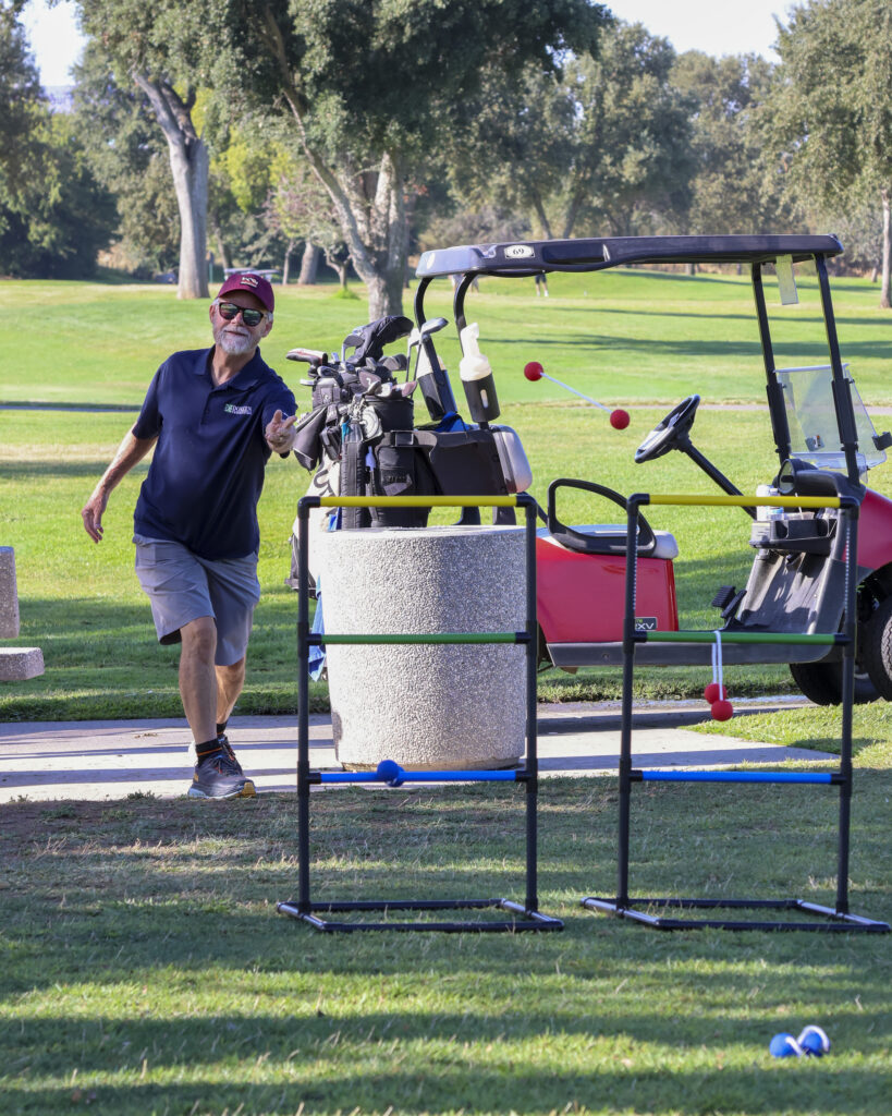 A golfer is playing ladder ball, throwing two balls connected by a rope toward ladders. There is already two balls wrapped around the middle rung of the ladder.