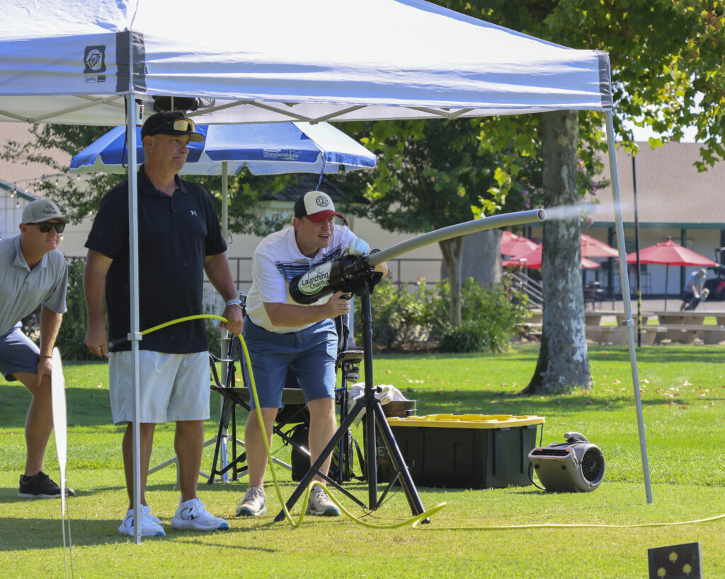 A golfer launches his ball with the ball launcher. A white gust is coming out of the launcher after shooting the ball.