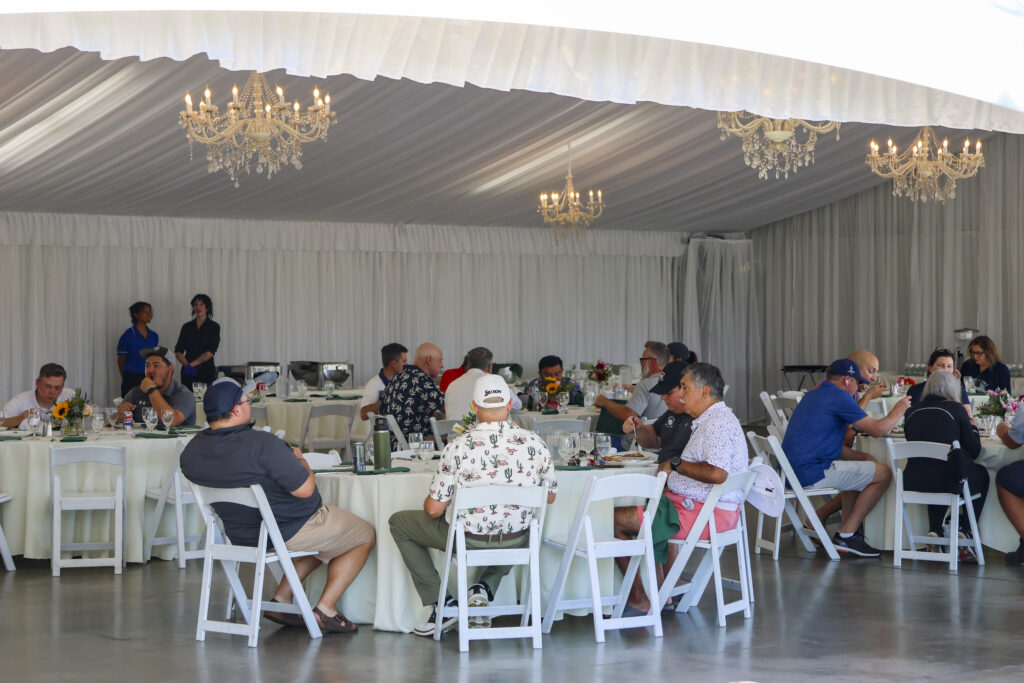 A large group of golfers having lunch in the Haggin Oaks Pavilion. There are 4 tables visible with 2-7 golfers sitting at each. 