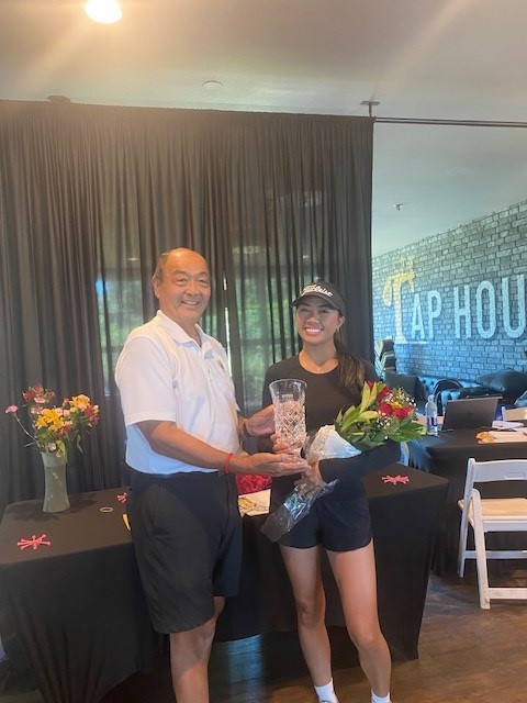 Erica Villegas smiling while holding the Womens Amateur State Fair Trophy and a bouquet of roses in the Bartley Cavanaugh Tap House alongside Charlie Cheung from the Sacramento Golf Council.