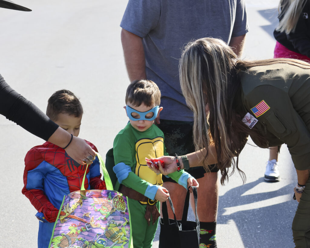 Two children dressed like Spiderman and a Teenage Mutant Ninja Turtle are getting candy from Brandy Legay, dressed in a pilot's jumpsuit.