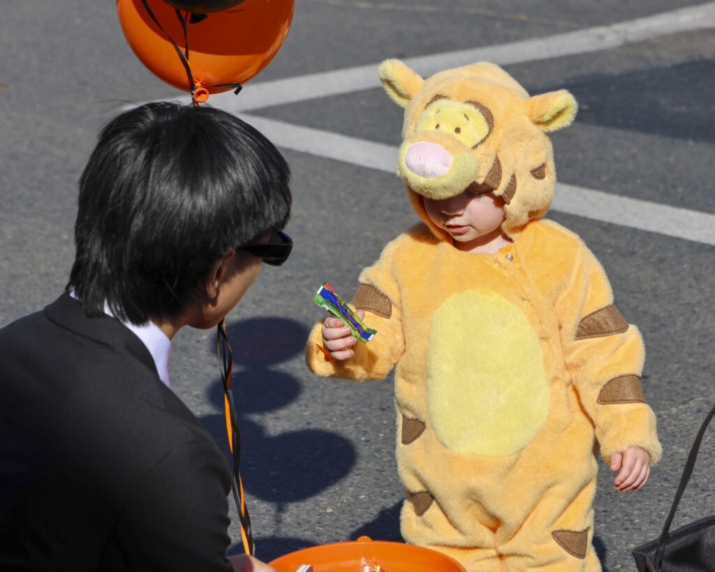 A child dressed like Tigger is holding a piece of candy he just got from a Morton Golf Foundation volunteer.