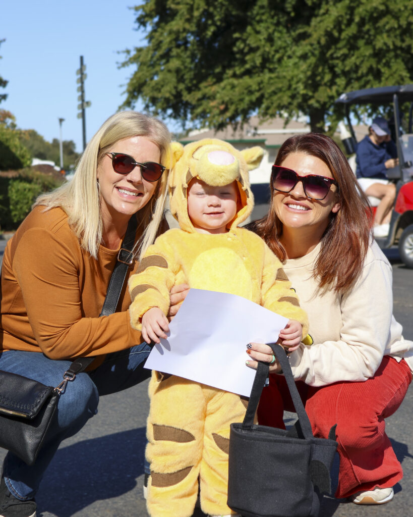 Two women crouch down to take a picture with a toddler dressed like Tigger from Winnie the Pooh.