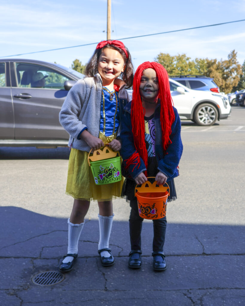 Two young sisters pose for a photo outside the parking lot. One is dressed like Snow White and the other is dressed like Sally from Nightmare Before Christmas with red hair.