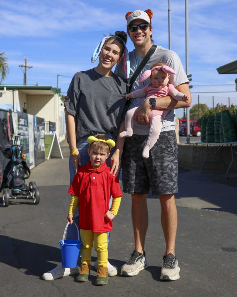 A family of 4 poses for a photo, dressed as characters from Winnie the Pooh. The son is Winnie, the baby is Pigley, the mother is Eeyore, and the father wears red Disney ears.