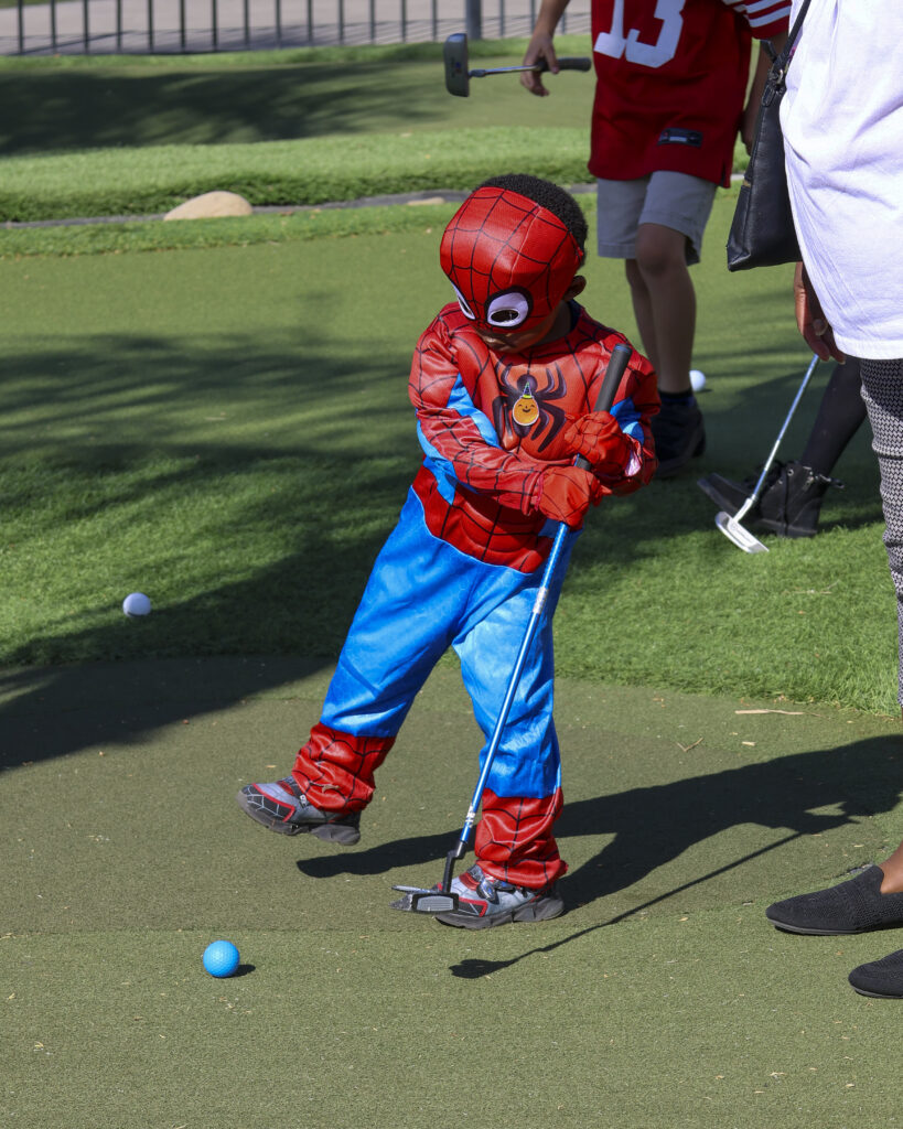 A child dressed like Spiderman is putting on the MacKenzie Putting Course.