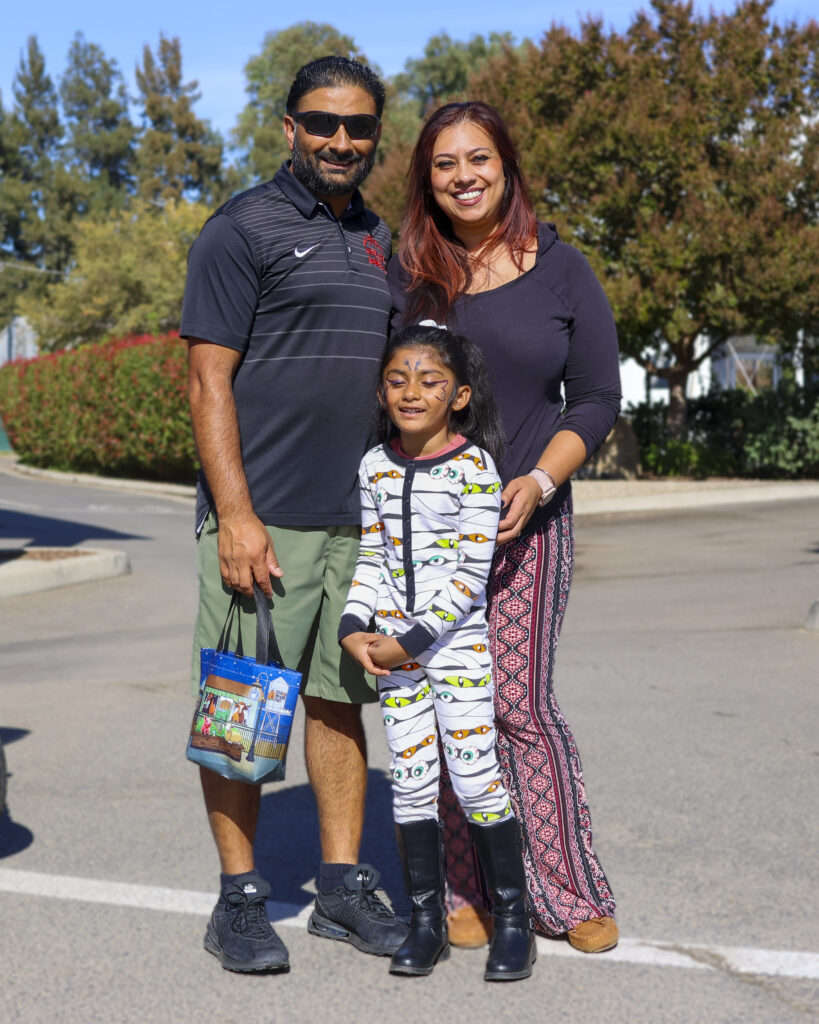 A family of 3 poses for a photo. The parents are in regular clothing while the daughter is dressed in white pajamas with a colorful pattern.