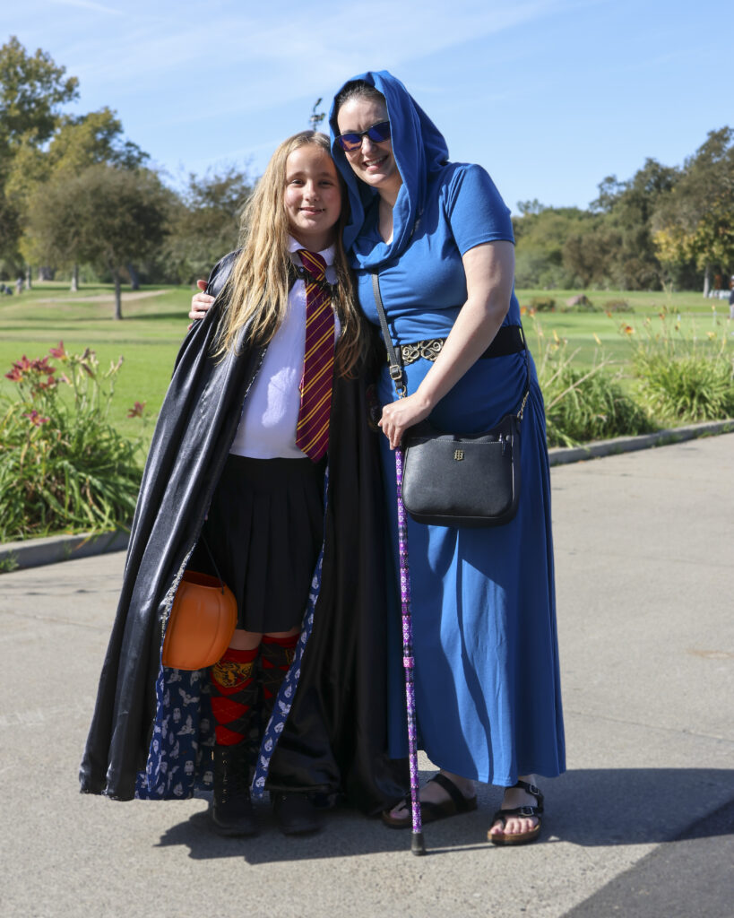 A mother and daughter pose for a photo. The daughter is dressed like a Gryffindor student from Harry Potter and the mother is dressed like a wizard in a blue robe.