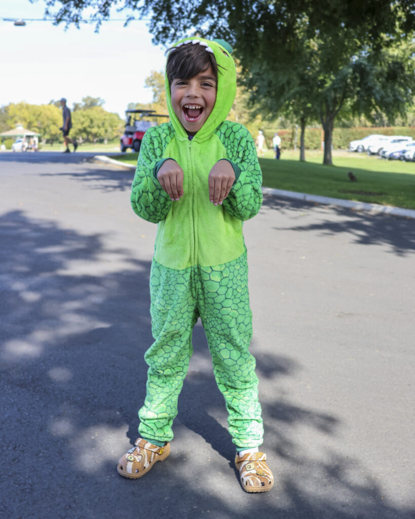 A young boy poses like a T-rex for a photo in a dinosaur costume.