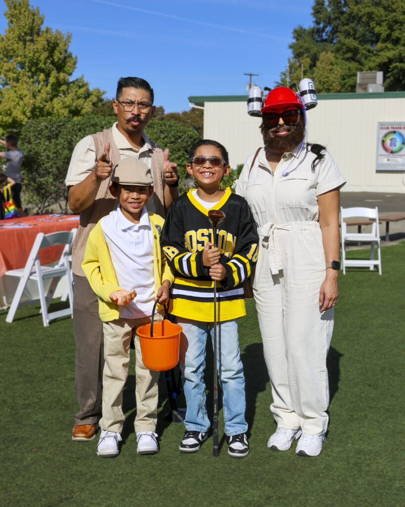 A family of 4 poses for a photo while dressed up as Happy Gilmore characters. One son is in a hockey jersey like Happy Gilmore, another is dressed like Chubbs, the mother is dressed like Happy's caddy, and the father is also dressed like Chubbs.