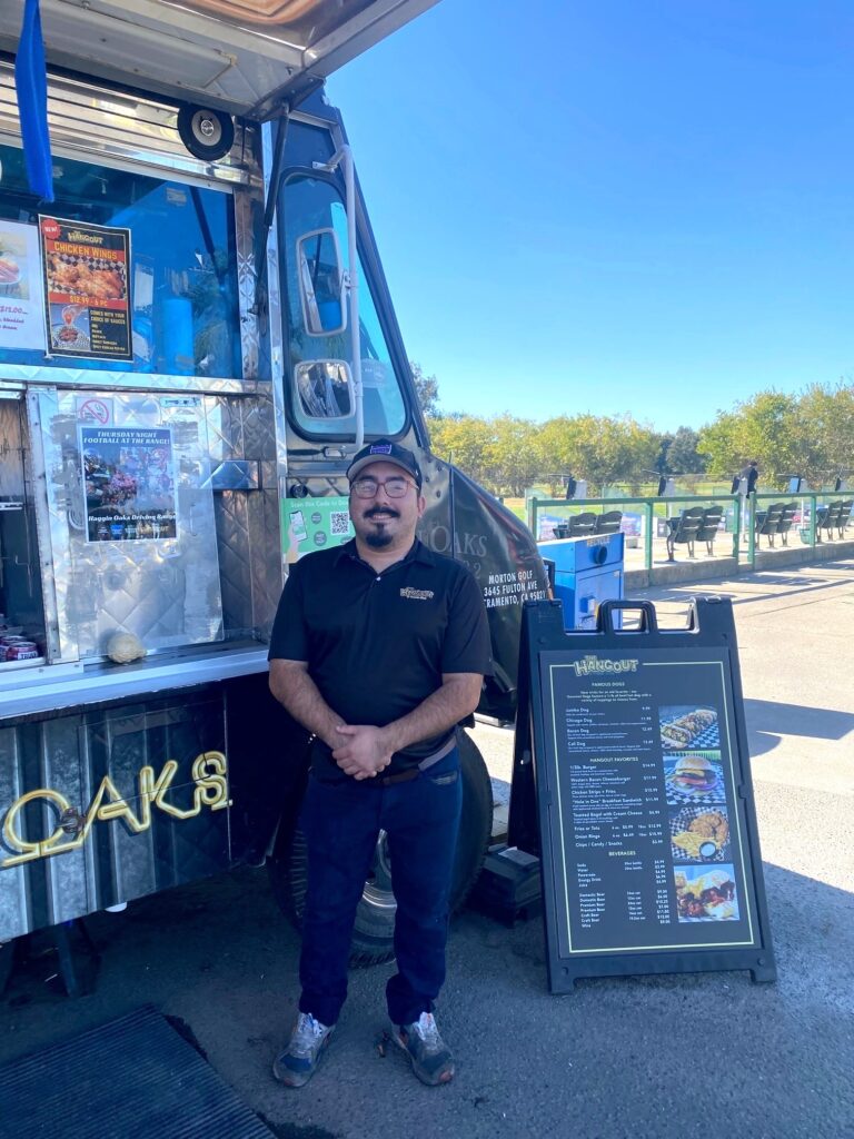 Man in hat and glasses standing in front of food truck