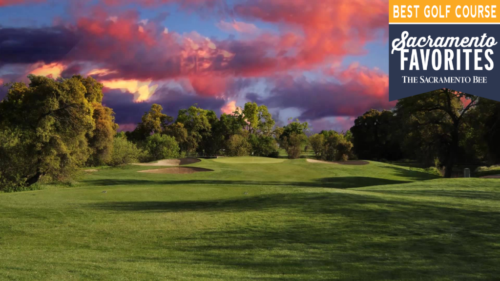 A wide view of the #16 hole on the MacKenzie Course at Haggin Oaks. In the distance is the pin with the flag, with violet and purple clouds in the sky at sunset.